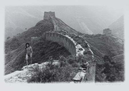 A black and white photograph of a young androgynous naked person (the artist Ma Liuming) walking on top of the Great Wall of China.