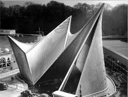A close-up view of a large, modern architectural structure with sharp, angular forms and a distinctive design, set against a backdrop of trees.